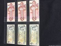 3 Canadian $2 bills from 1986, each individually sleeved, featuring Queen Elizabeth II and a reddish-pink color scheme.