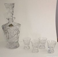 Full view of Bohemian lead crystal decanter with stopper and four shot glasses arranged in front.