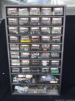 Full view of black multi-drawer organizer filled with assorted small hardware components including bolts, rivets, hinges, and various metal parts in each drawer.