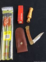 Full view of bird call, knife with sheath, knife box, and packaged shotgun cleaning rod on black background
