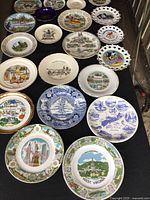 Top view of 22 assorted ceramic/porcelain souvenir plates with various U.S. state and historic themed illustrations and colors.