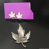 Front view of brooch and earrings mounted on purple card, showing detailed textured pewter maple leaf brooch and small rhinestone maple leaf earrings.