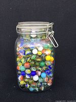 Front view of a large glass jar filled with colorful assorted marbles showing colors and variety inside.
