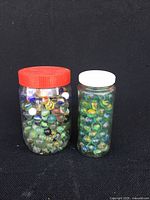 Two glass jars filled with assorted multicolor glass marbles, one with red lid, one with white lid.