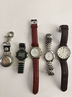 Full view of all 5 watches including pocket watch on left and 4 wrist watches aligned horizontally showing different bands and faces.