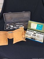 Socket wrench set in plastic case, leather tool belt, and Hilka tap and die set in metal case.