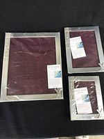 Set of three pewter picture frames on black background with protective covers and informational card visible in each frame.