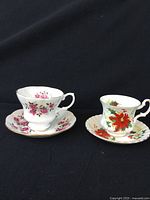 Two Royal Albert bone china teacups and saucers with distinct floral patterns: one pink roses, one poinsettia.