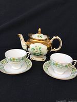 Teapot with two teacups and saucers arranged showing floral and gold design