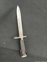 Full view of US Military M6 bayonet showing blade and textured plastic handle on dark background.