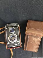 Top view of Yashica-A camera next to brown leather case, highlighting the camera body texture and case details