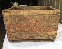 Front side of vintage Coca Cola wooden crate showing faded red Coca Cola logo on weathered wood.