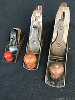 Front view of three vintage hand planes showing different sizes and wooden handles, some rust visible on blades and metal parts.