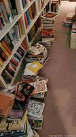 Long view of multiple stacks of cookbooks on floor beside bookcases