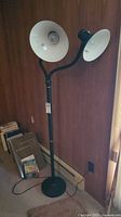 Full view of black floor lamp with two shades standing near wall