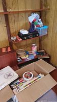 Wide view of shelf and box showing Lego bin, board games, badminton rackets, flower drying kit