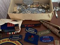 overview of box with coins, buttons, dog tag, patches spread on surface