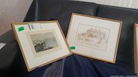 Both framed prints leaning on sofa, showing frames and matting