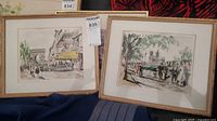 Two framed street-scene prints with light wood frames and mats