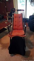 Front view of black wooden rocking chair with orange cushions and black lumbar cushion