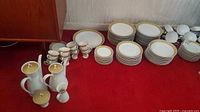 Stacks of dinner plates, salad plates, side plates, bowls, cups, saucers, and tall pots displayed on red carpet