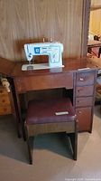 Singer Stylist sewing machine on cabinet with stool in front