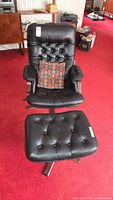 Full view of black tufted swivel chair, ottoman and pillow