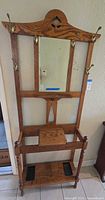 Front view of antique wooden hall tree showing hooks, mirror, small shelf, and upper section design.