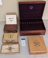 Photo showing five vintage cigar boxes and one open wooden silverware chest with velvet interior and compartments.
