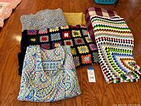 Photo shows Vera Bradley tote bag with seven blankets and shawls folded and laid on wooden floor.