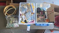 Overview photo showing four plastic totes filled with fabric scraps, embroidery hoops, beads, buttons, and other craft items on a table.