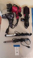 All five hair styling tools arranged on table: two hair dryers, one volumizer brush, two curling irons