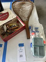 Lot with vintage wooden fishing net, Swisher Sweets cigar box with fishing lures, and plastic tackle box with hooks on table