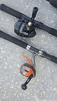 Close-up photo of two fishing rods showing Zebco reels - one black baitcasting style and one bright orange spinning reel, both mounted on rods with foam handles.