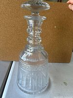 Cut glass decanter with stopper on a flat white surface, clear intricate design visible