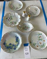 Overview of 2 porcelain salt and pepper shakers with gold-tone tops and 6 matching hand-painted floral porcelain plates with scalloped edges and gold trim.