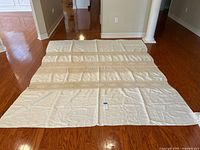 Full view of the ivory linen tablecloth laid flat on a wood floor showing overall size and shape.