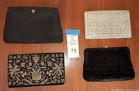 Top view of four ladies clutch style evening bags arranged on a table: black suede with gold clasp, cream patterned clutch, black embroidered clutch, black velvet fringe clutch.