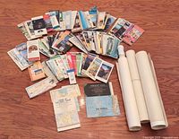 Wide angle photo of assorted folded and rolled maps spread on the floor showing a large collection of individual maps including road and topographic maps.