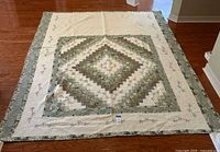 Full view of quilt spread out flat on wooden floor showing central diamond patchwork pattern surrounded by wide white and green floral borders