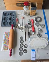 Full view of Maid of Honor vintage cookie press set and accessories on table, including cookie press, box, metal discs, cutters, measuring cup, rolling pin, and doilies.