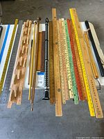 Overview of lot on table showing variety of wooden and metal measuring tools, dowels, and accessories including back scratcher and pencils.