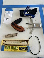 Overview of all pocket cutters and knives included in lot arranged on a white surface.