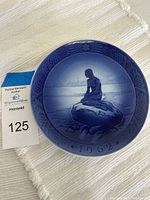 Top view of the blue and white Royal Copenhagen collector plate featuring The Little Mermaid sitting on a rock, dated 1962.
