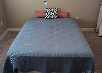 Queen mattress and box spring covered with fitted sheets and blue quilted coverlet with throw pillows on top