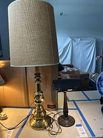 Wide view showing two lamps on table, the tall brass lamp with burlap shade and the shorter brass banker’s lamp with green glass shade.
