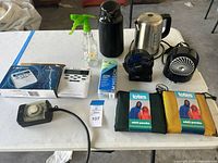 View of all items on table including ponchos, fans, cooling towel, kettle, thermos, spray bottle, and power timer