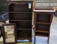 Three wood pieces including two dark brown traditional style wall shelves and a wall mirror. Large shelf with decorative trim, smaller shelf with raised tray top and legs, mirror rectangular with wall hanger.