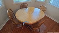 Dining table with four Windsor chairs arranged around it, showing oval shape and leaf in place.