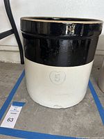 Full view of the vintage 5 gallon crock showing its height, black top glaze, and tan body with heart symbol.